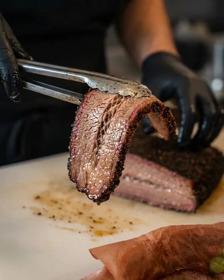 A gloved hand lifting a slice of brisket off the board