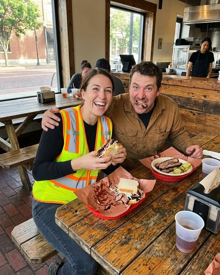 Two regulars on a lunch break, smiling over trays of barbecue at a wooden table
