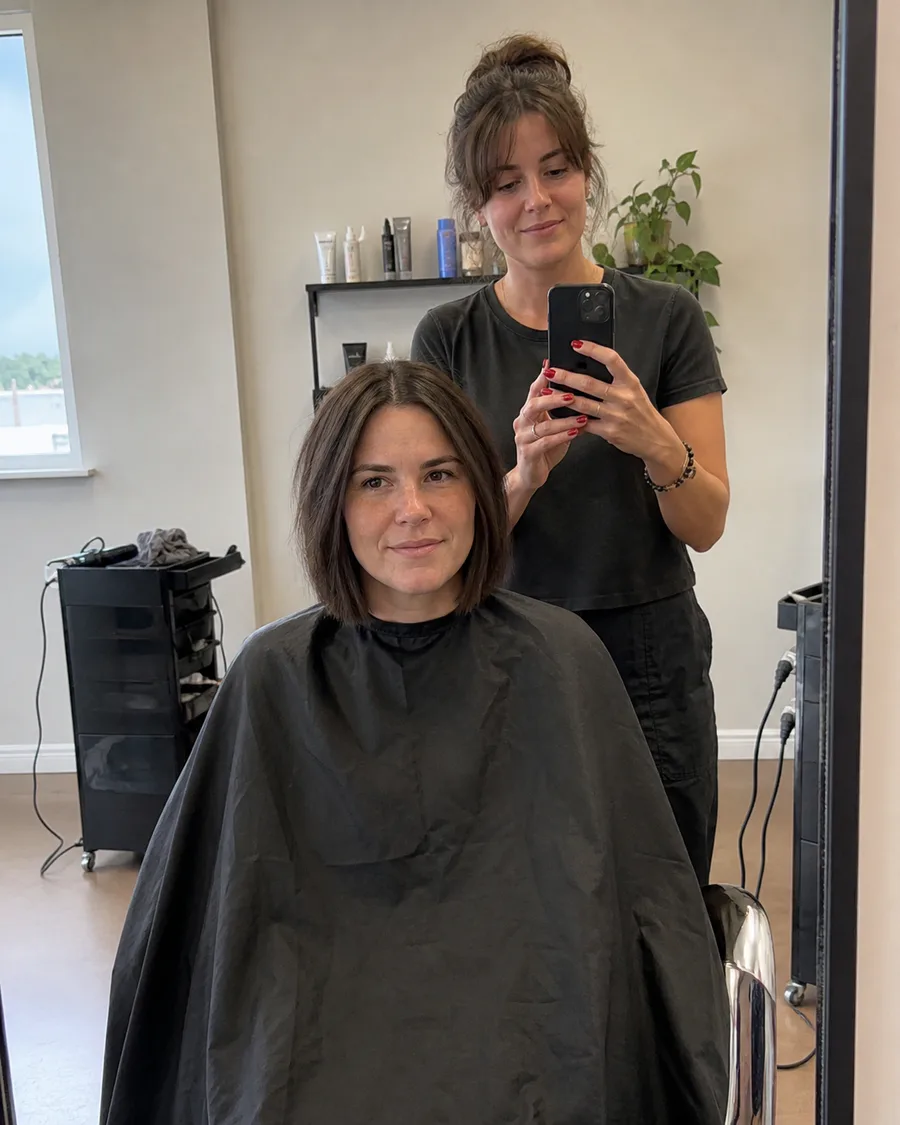 A stylist photographing a client in a black cape in the salon mirror