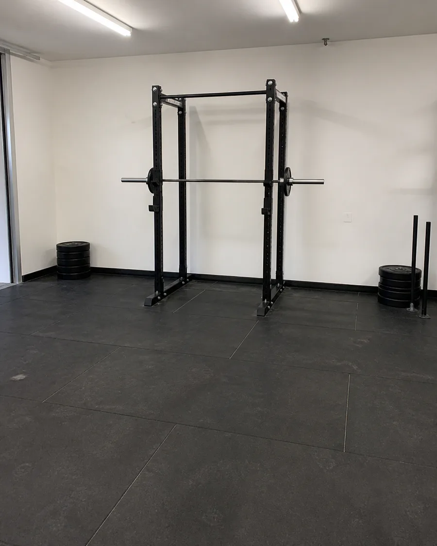 Phone photo of an empty gym corner with one squat rack and black rubber flooring